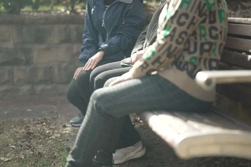 Three women sitting on a park bench.