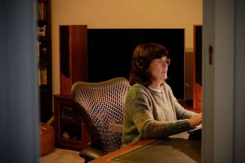 A woman is seen through a door sitting at a desk.