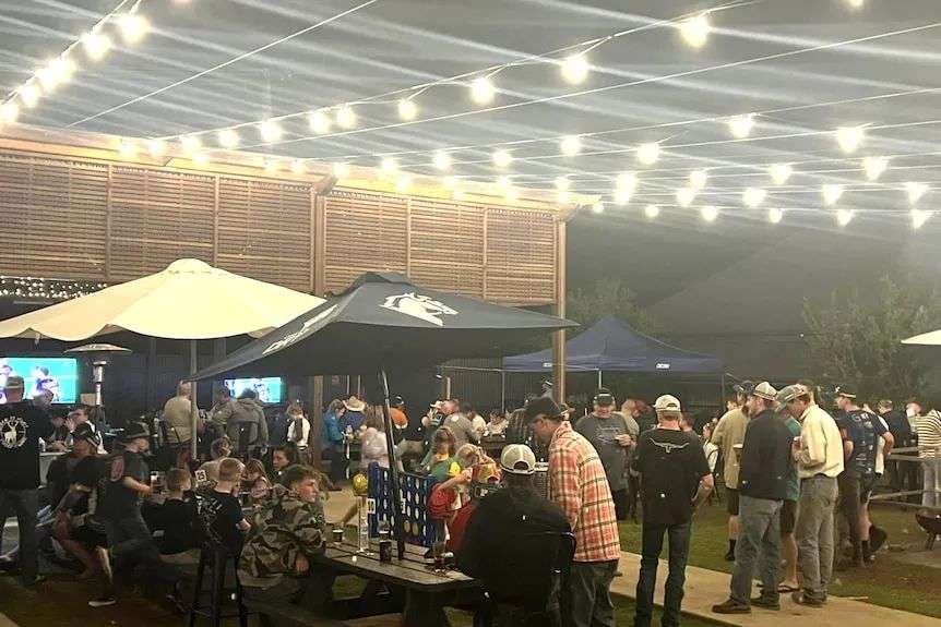 People gathered under festoon lights, black, cream patio umbrella, night time.