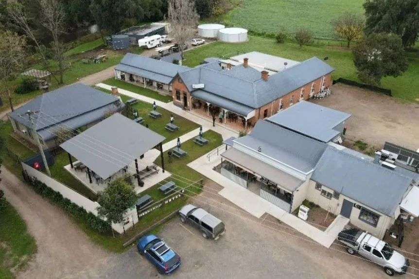 An overhead shot showing a couple of buildings, including a red historic one, cars parked in front. park, trees, green grass.