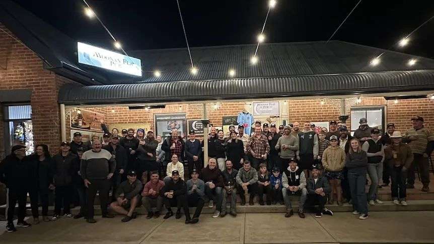 A large group of people gathered outside a red building, lights strung up, night.