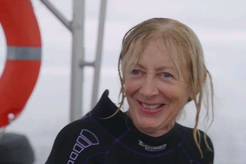 Woman in wetsuit on boat smiling as she talks to someone.