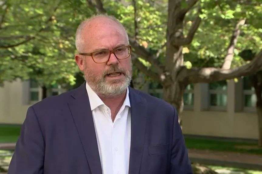 Senator Tim Ayres is talking as the photo is snapped. He is wearing glasses and his mouth is open.