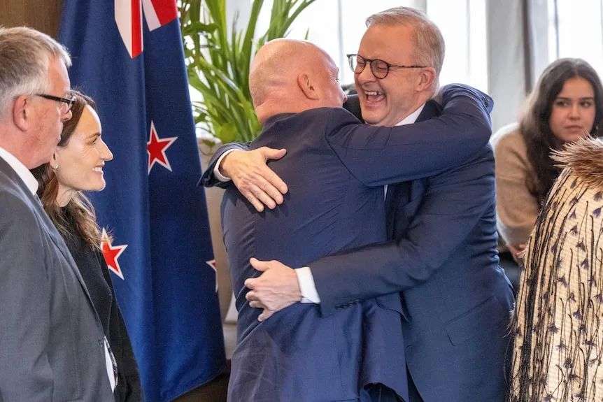 两名身穿深蓝色西装的中年男子互相拥抱，大笑起来。