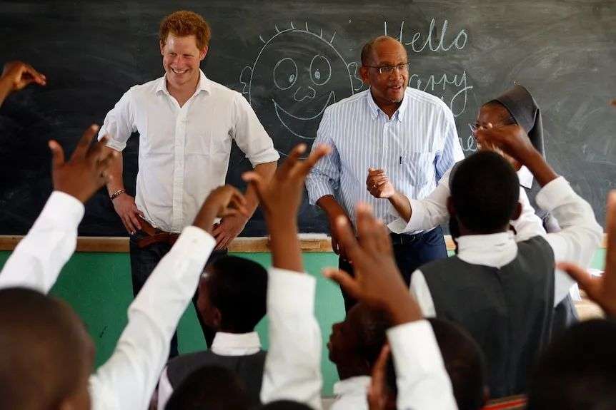 Prince Harry and Prince Seeiso smiling while standing in front of a classroom black board