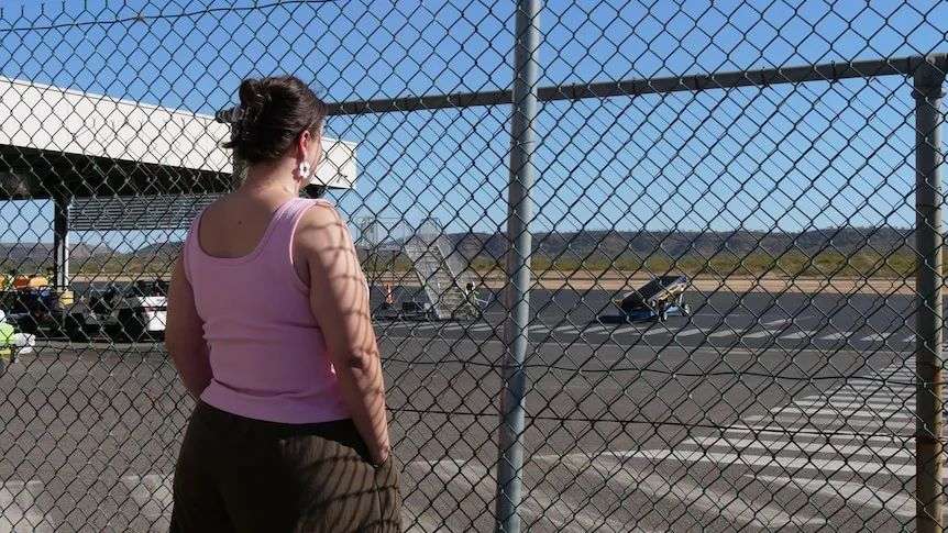 a woman standing in front of an airport fence looking at the runway