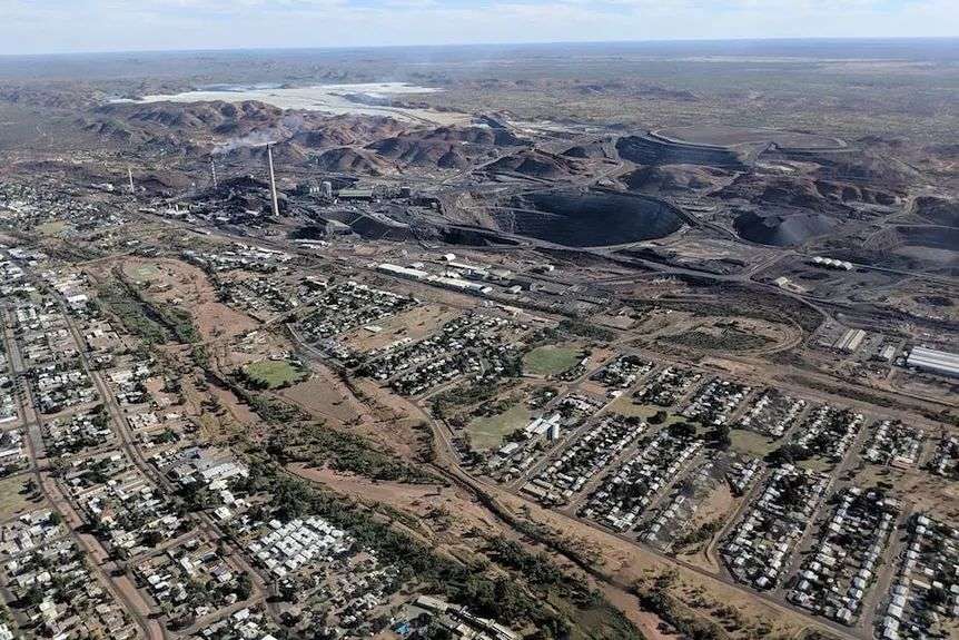An aerial view of a township, with greenery, blue skies and ocean in the horizon.