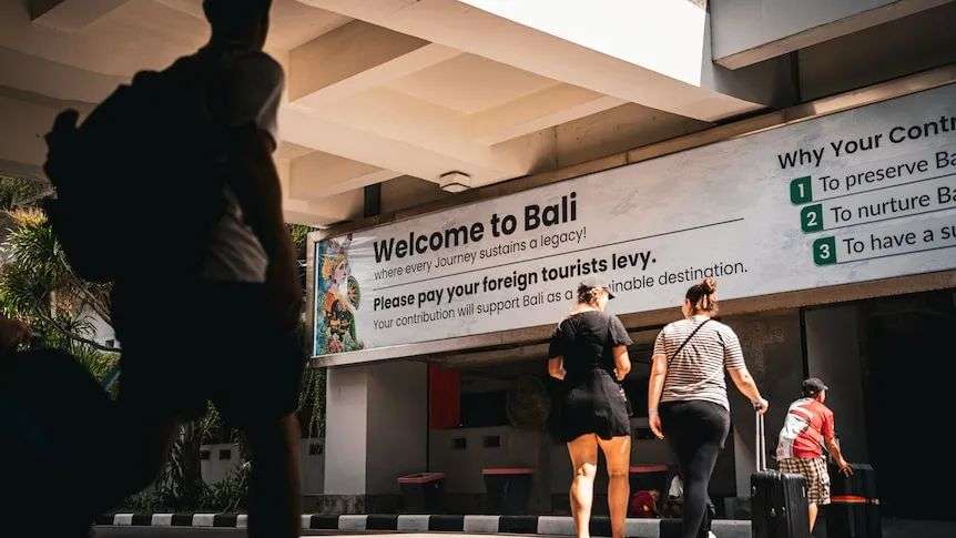 A group of people walk passed a sign that says Welcome to Bali.