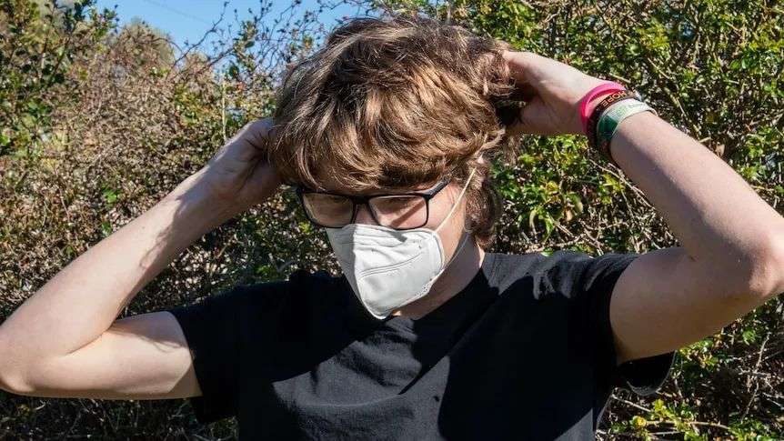 A teenage boys with glasses puts on a face mask out in a garden