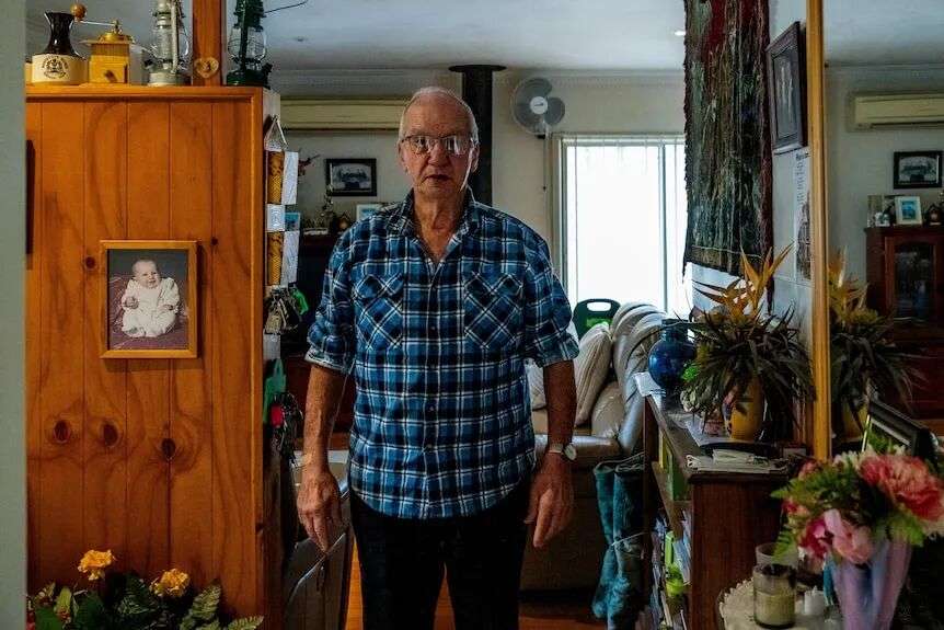 一名男子身穿蓝色格子衬衫,站在客厅里,背景中挂着一张婴儿的照片。