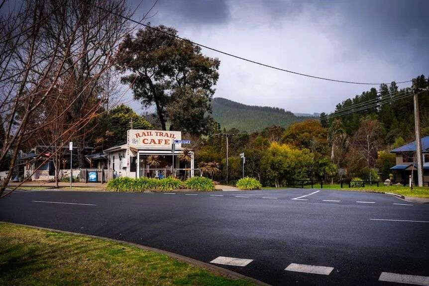 空旷道路拐角处的“铁路小径咖啡馆”照片,背景是森林覆盖的群山
