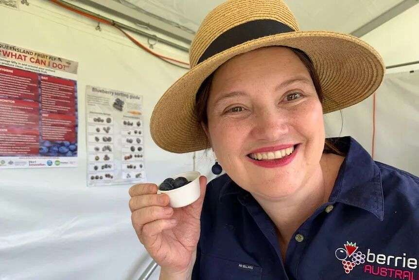 A woman smiles as she holds a small cup of blueberries.