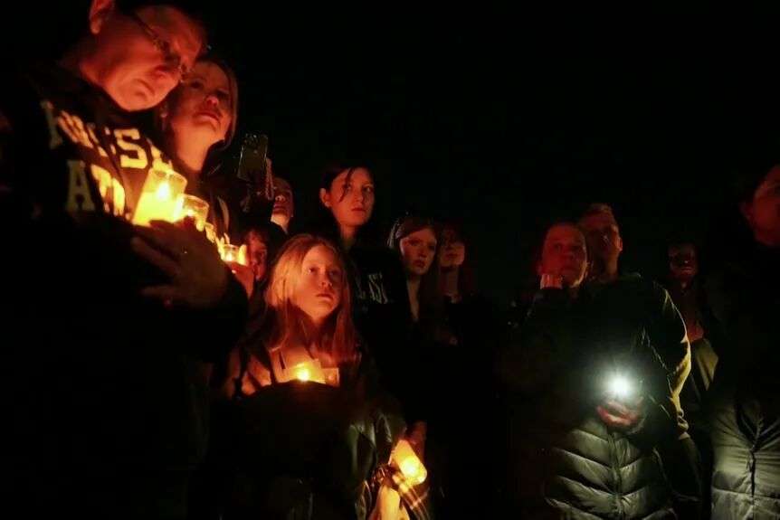 一群哀悼者在漆黑的夜空背景下手持蜡烛。