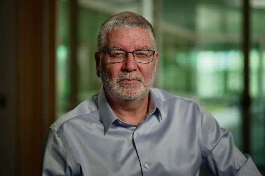 Nigel McMillan wearing a grey shirt looks at the camera.