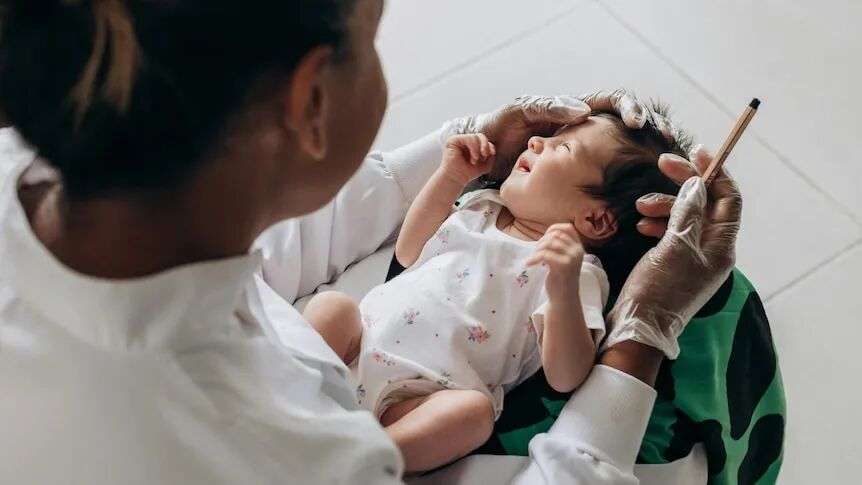 A generic photo of a baby lying in the lap of a doctor who is holding syringe.