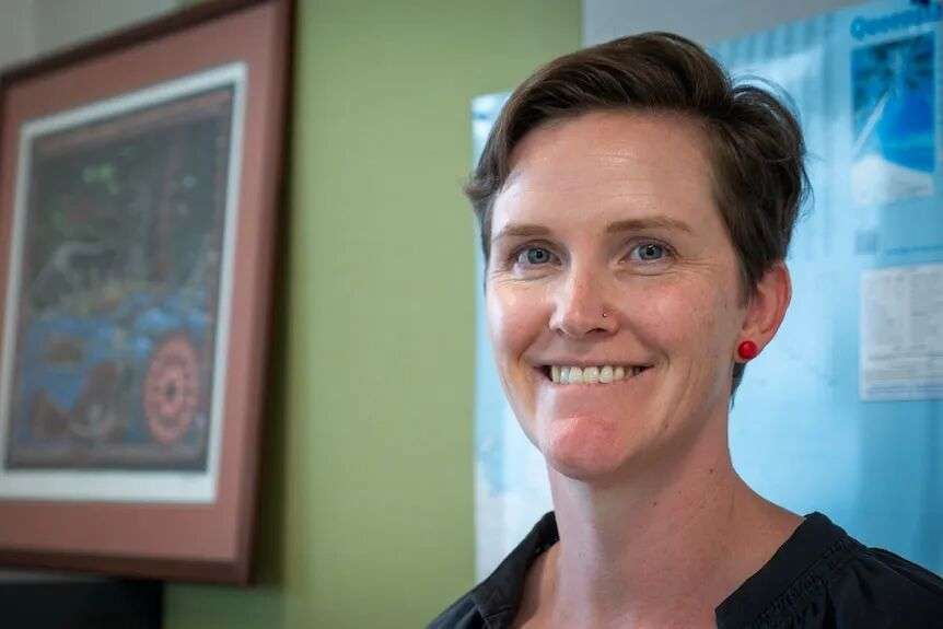 Portrait of woman in office with aboriginal art framed behind.