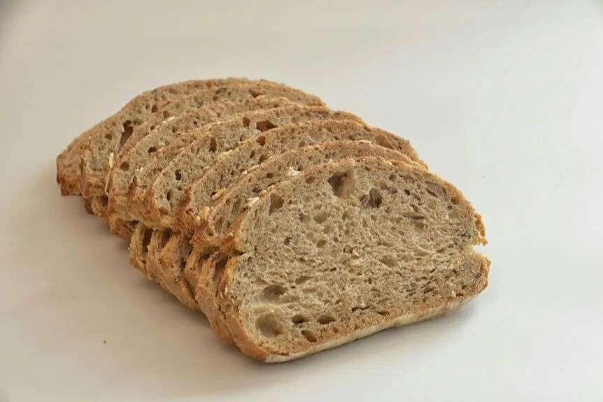 Slices of mutigrain bread lay on top of each other on plain surface.