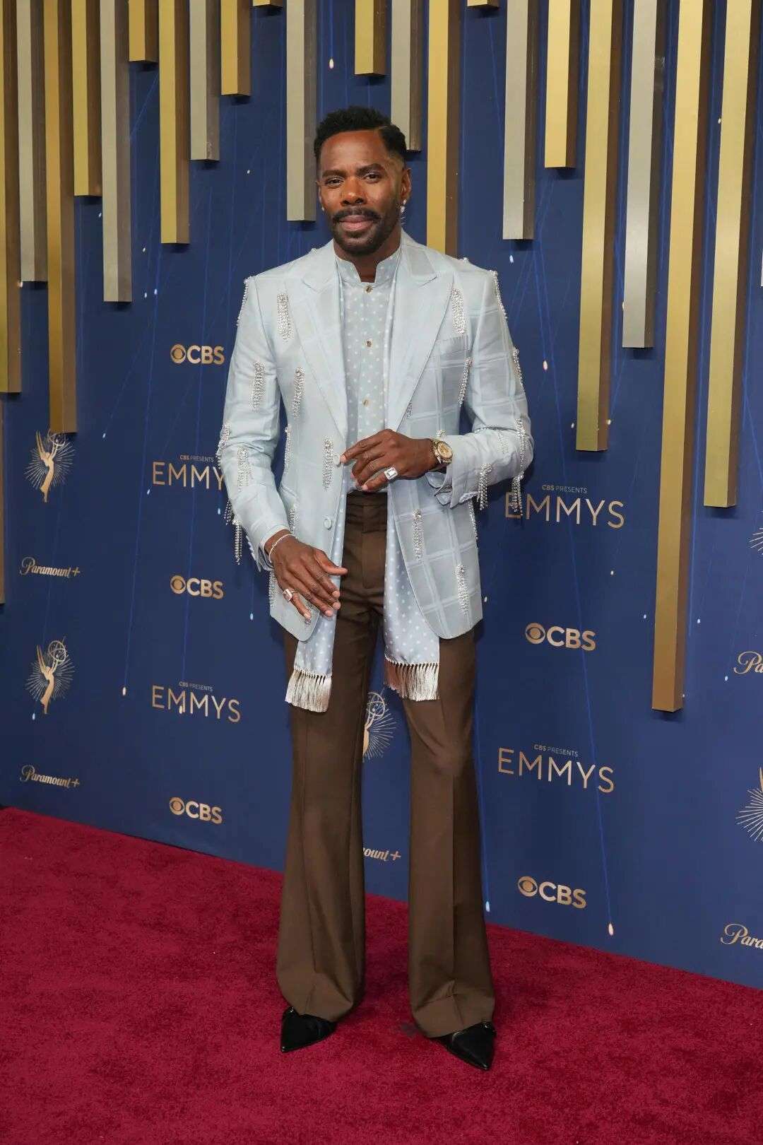Colman Domingo wearing a pale grey blue suit jacket with matching scarf and brown trousers