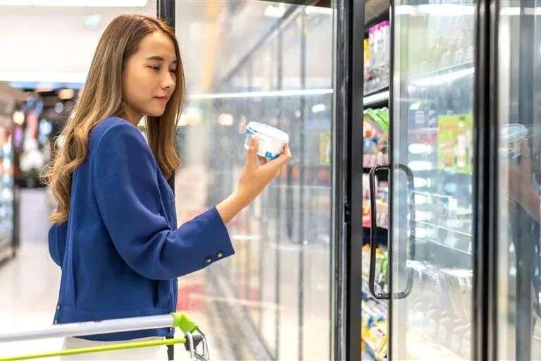 A woman choosing a dairy product from a supermarket fridge section