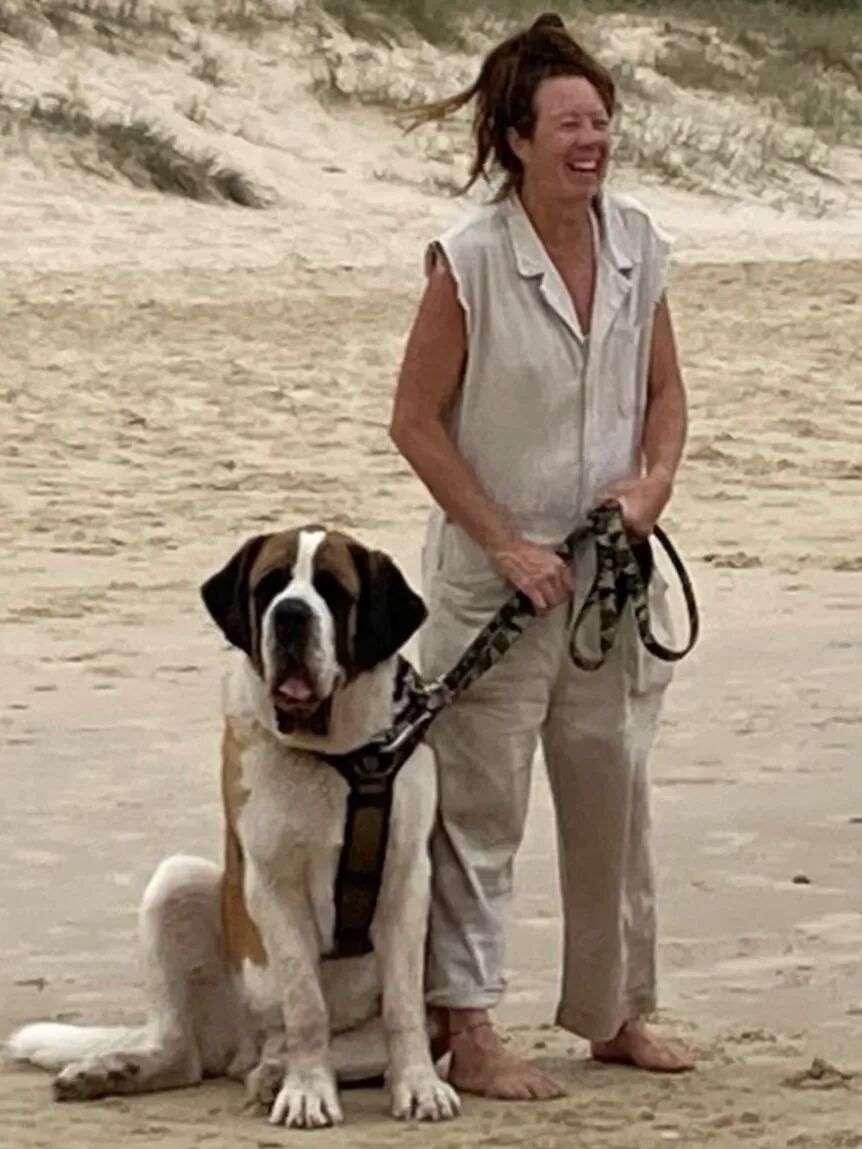 A middle aged lady standing next to a dog on the beach