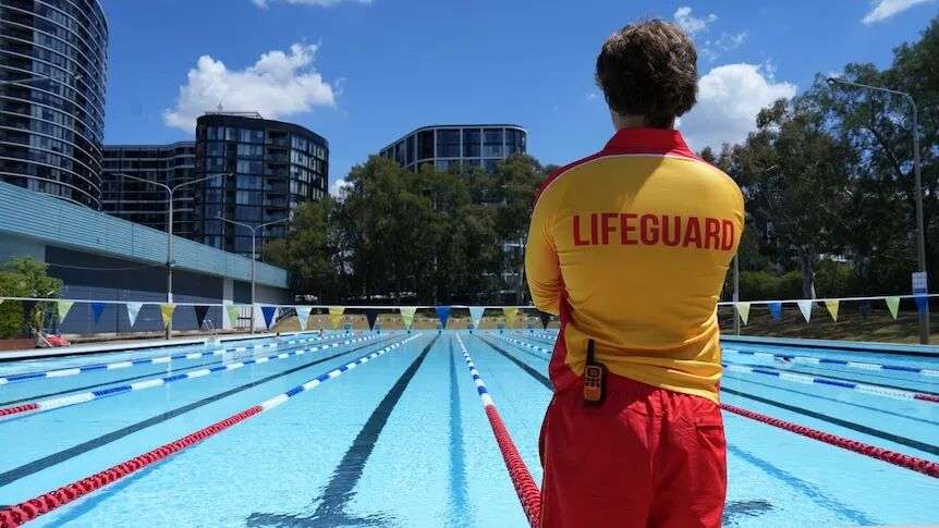 The back of a lifeguard standing in front of an empty swimming pool.