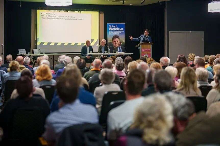a crowd sits and watches people speaking on a stage