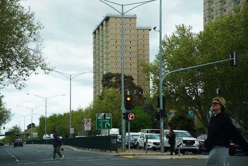 pedestrians walk across a busy road in front of an old public housing tower