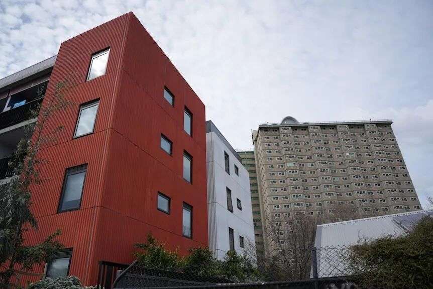 A modern red multi-storey apartment block beside an older, light brown multi-storey apartment block.