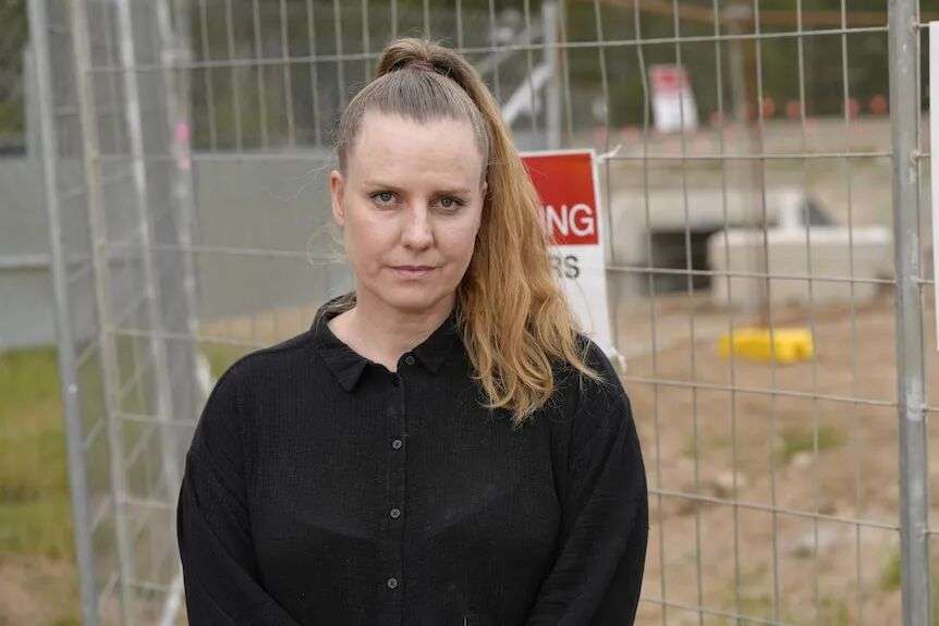 A woman with long hair wearing a black shirt stood in front of a fence