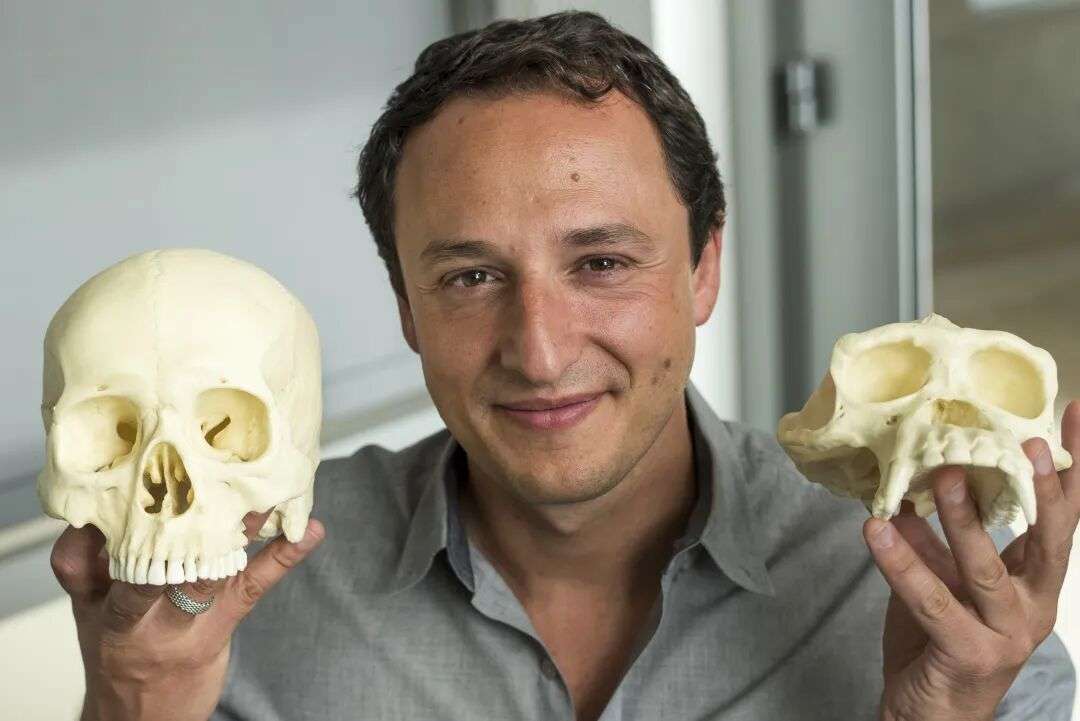 A man holds two casts of skulls in each hand and smiles at the camera