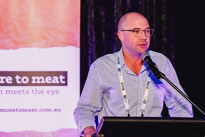A man in glasses stands at a lectern and delivers an address.