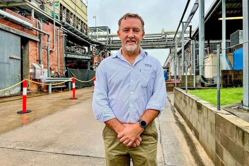 A man wearing a check blue and white collared shirt and khaki trousers stands in the walkway of an abattoir.