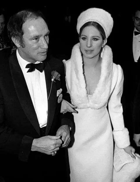 He wears black tie and she wears white dress and hat