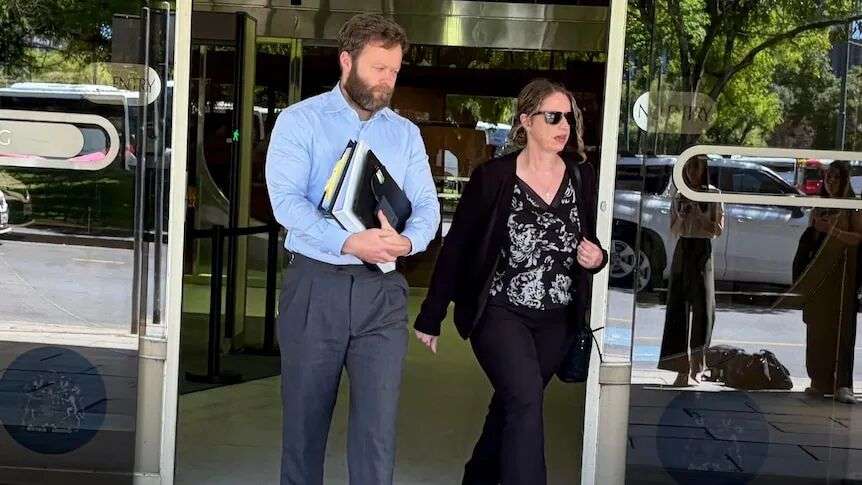 A woman and a man walk through glass doors, leaving a building