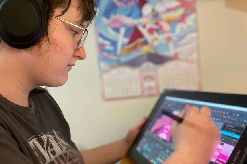 A woman wearing headphones and in a t-shirt draws using a drawing program on a screen.
