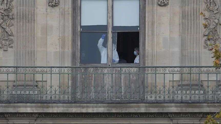 Police officers work inside the Louvre museum scrubbing a window for prints.
