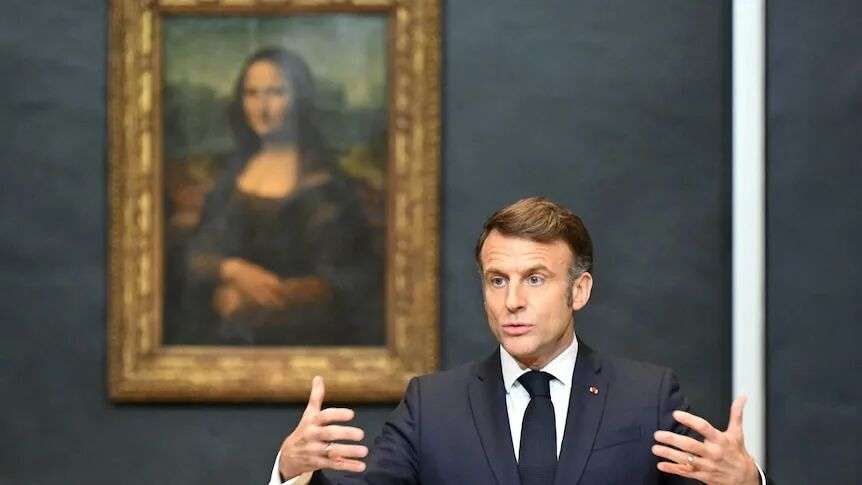 Emmanuel Macron gestures with his hands while standing in front of the Mona Lisa.