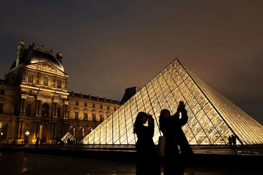 The glass pyramid entrance to the Louvre is lit up at night-time.