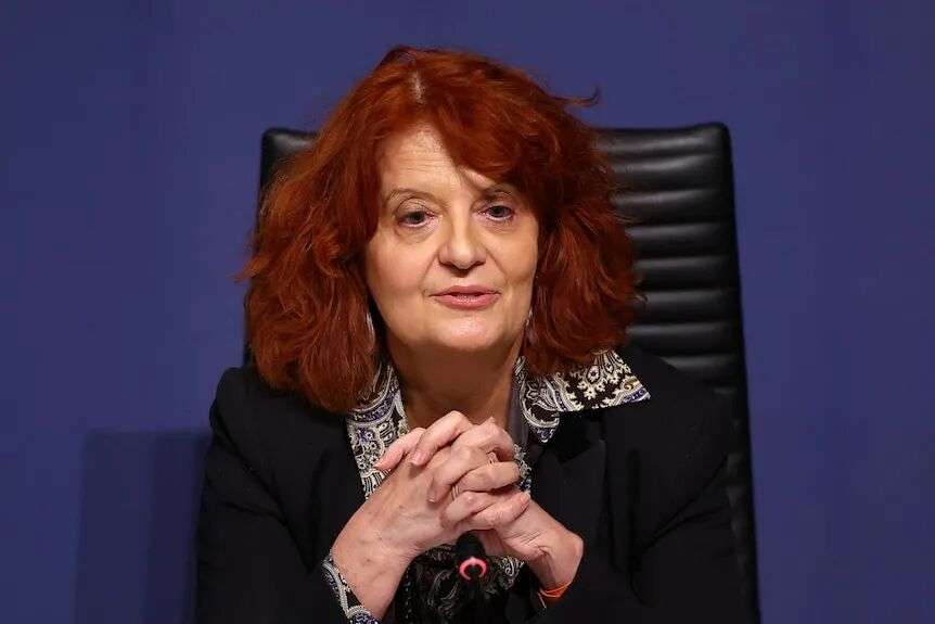 A woman with red hair speaking into a microphone at a press conference.