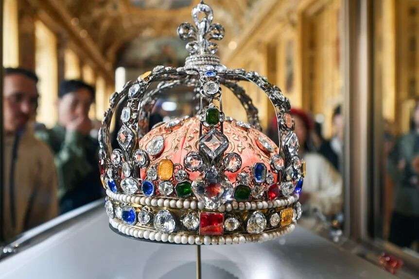 A silver crown encrusted with diamonds and mutli-coloured jewels sits in a glass case.