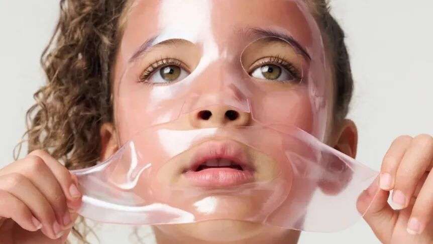 A young girl placing a pink-coloured, gel sheet mask over her face