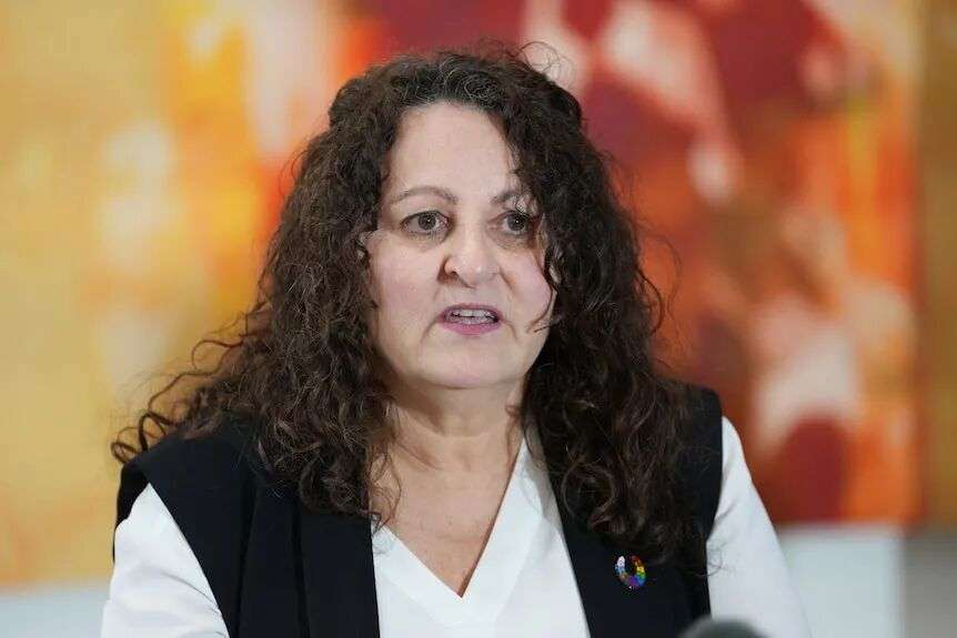 A woman in a white shirt looks seriously ahead.