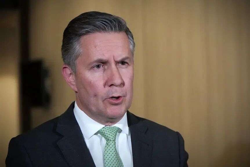 Mr Butler speaks in front of a beige wall.