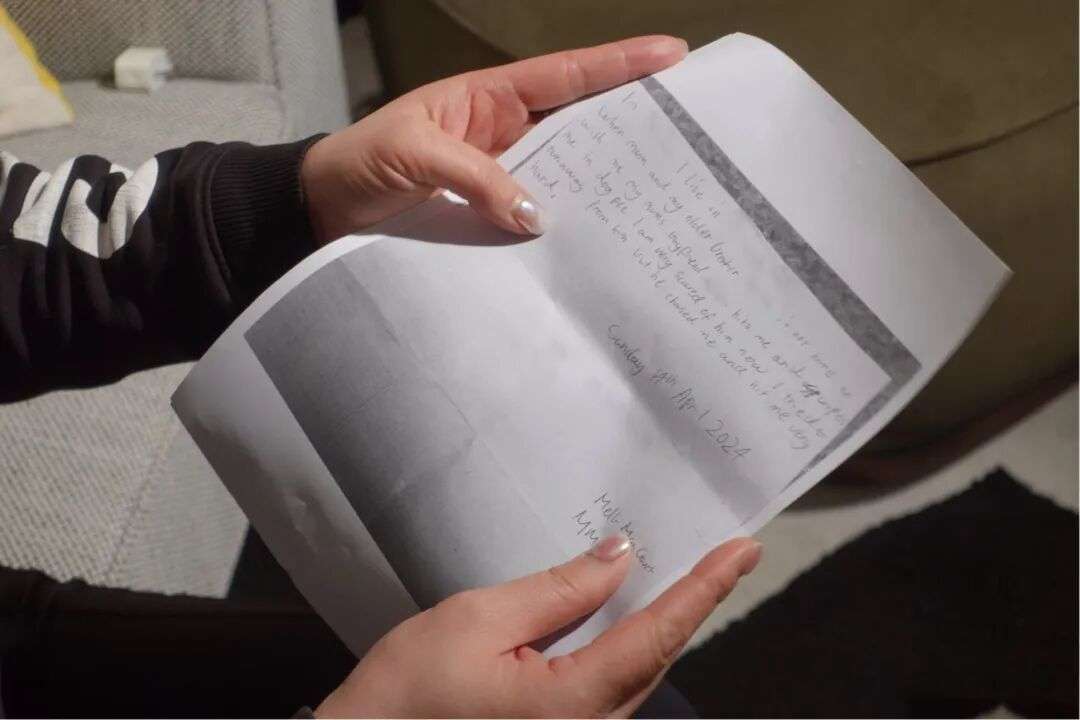 A person holds a handwritten letter with parts of the main body text blurred.
