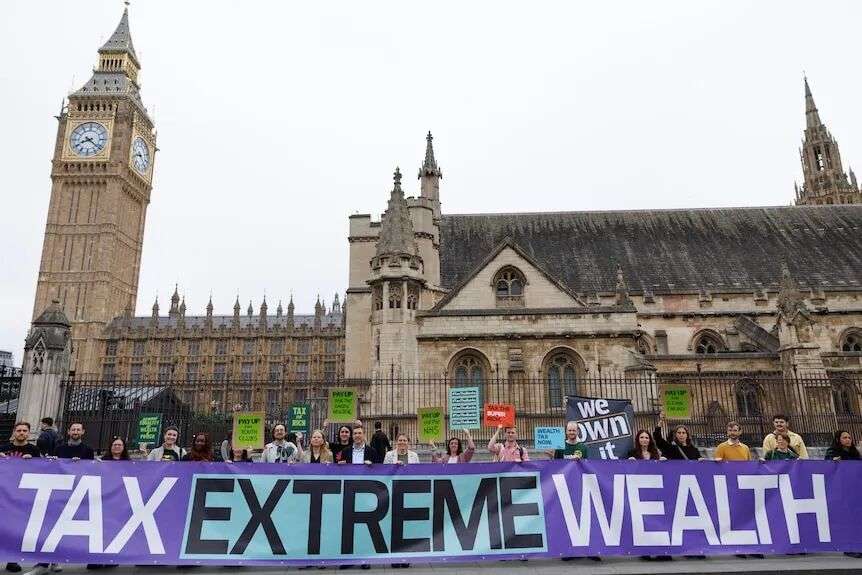 A group of people are holding a banner that says 'Tax Extreme Wealth'. The Big Ben clock is behind them.