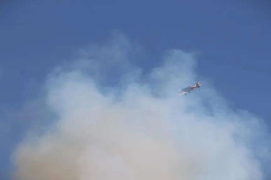 一架固定翼水上飞机穿过丛林大火产生的灰色烟雾，飘过蔚蓝的天空。