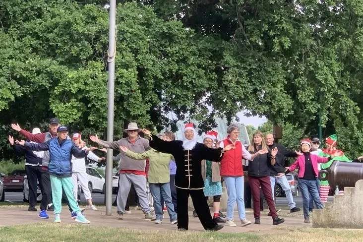 A group of people doing tai chi in the park, some dressed as Santa Claus and elves.