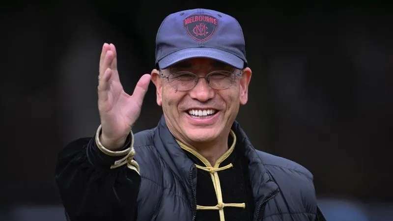 Man with glasses smiling wearing tai chi uniform and a Melbourne Demons Football Club hat.
