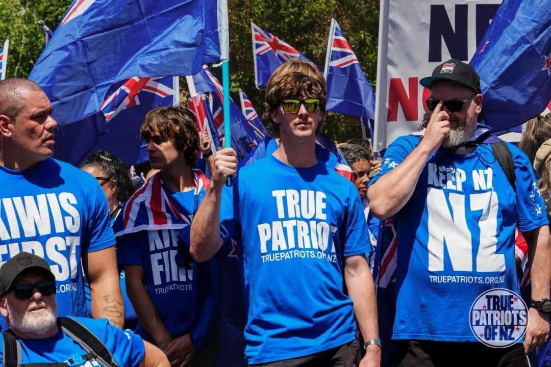 可能是包含下列内容的图片:人群和上面的文字是“N N WIS سلای NK HS S .ORZ FIl. TRUFATRIOTS TRUE PATRIO TRUEPATROTS.OhNZ REEPN1 NZ TRUEPATRIOTS. ORG.NZ TRU PATRIOTS OFNZ*”