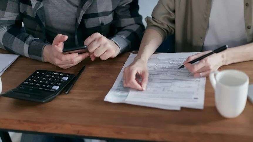 A couple seated at a table going over financial statements with a pen in hand and calculator nearby.